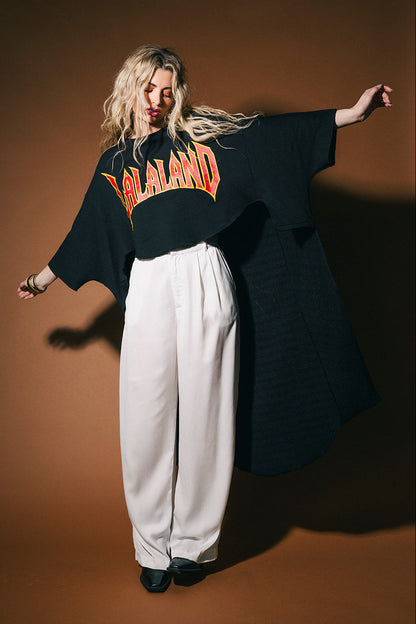 Person wearing a black sweater with 'LALALAND' text and white pants on a brown background