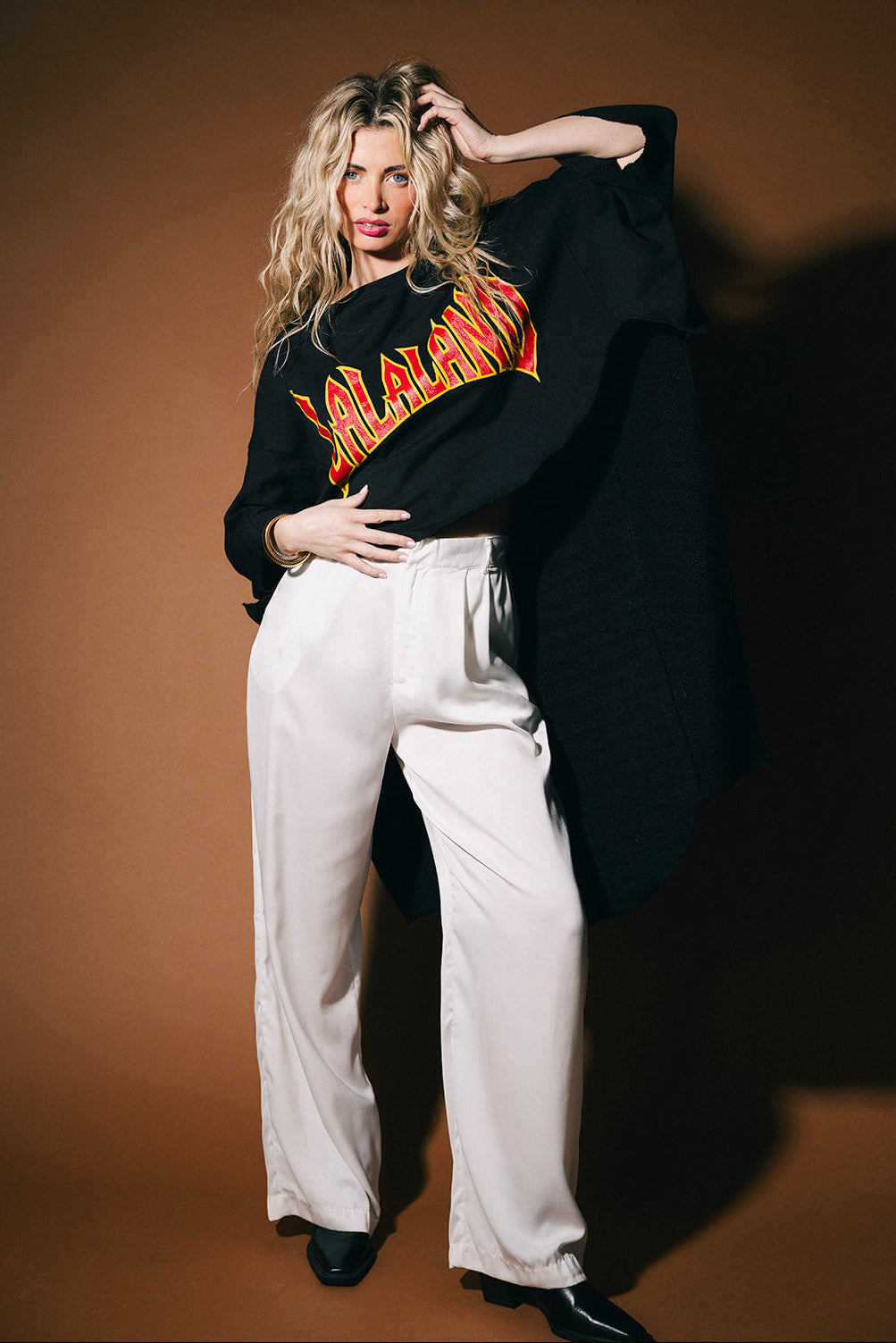 Woman wearing a black sweatshirt with red text and white pants against a brown background