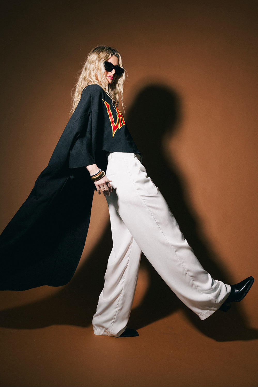 Person wearing a black coat and white pants against a brown background