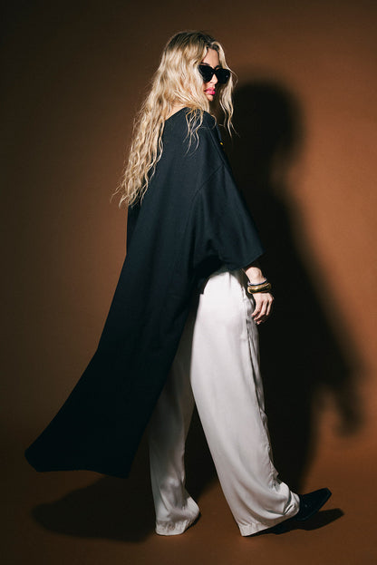 Person wearing a black coat and white pants against a brown background