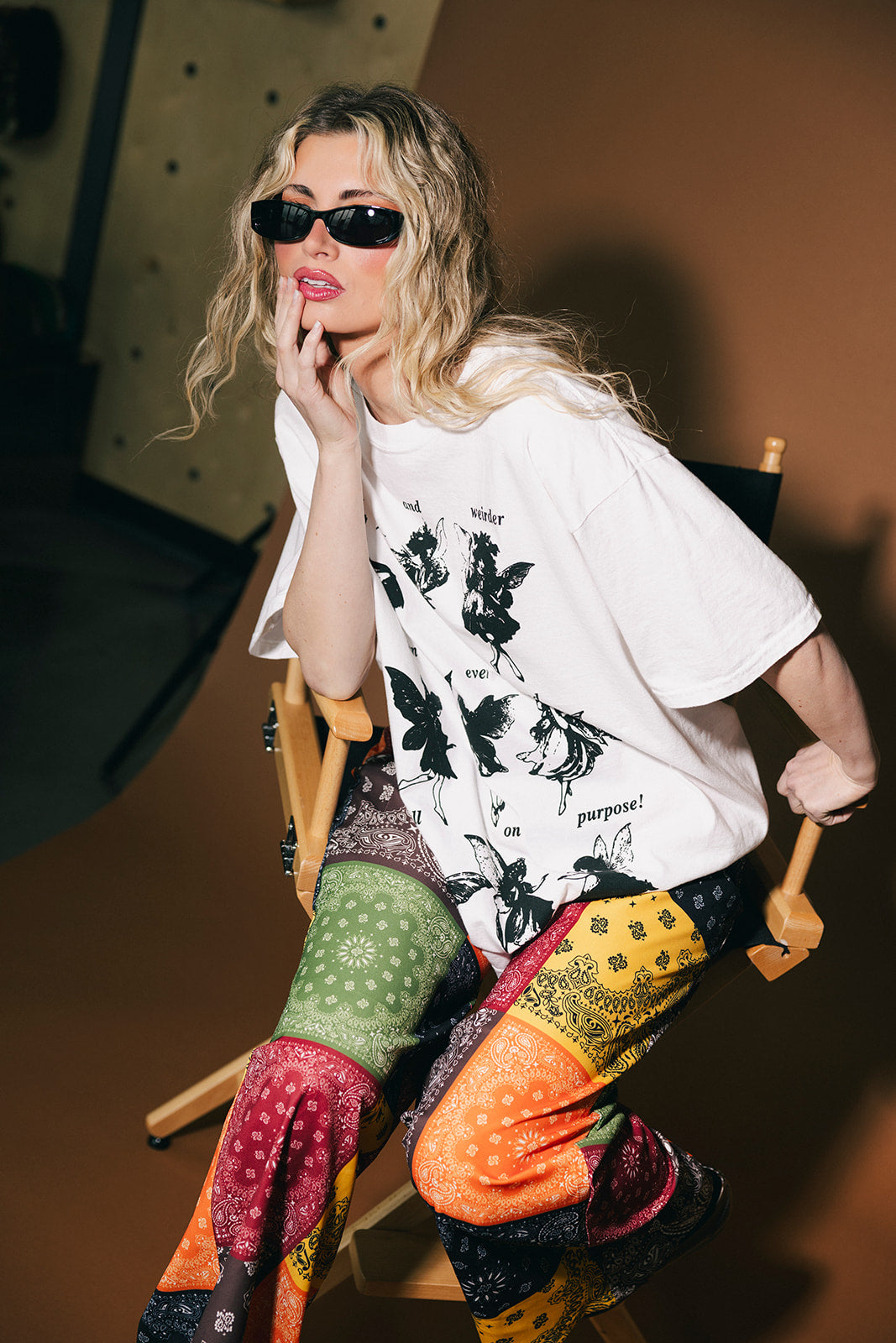 Person wearing a white t-shirt with black butterfly designs and colorful pants sitting on a chair.