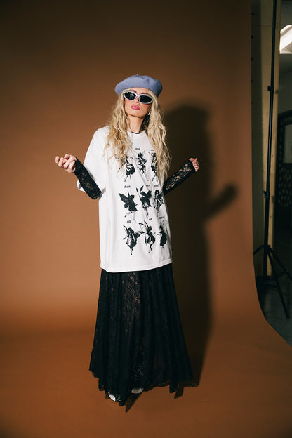 Person wearing a white t-shirt with black graphics and a black skirt against a brown background