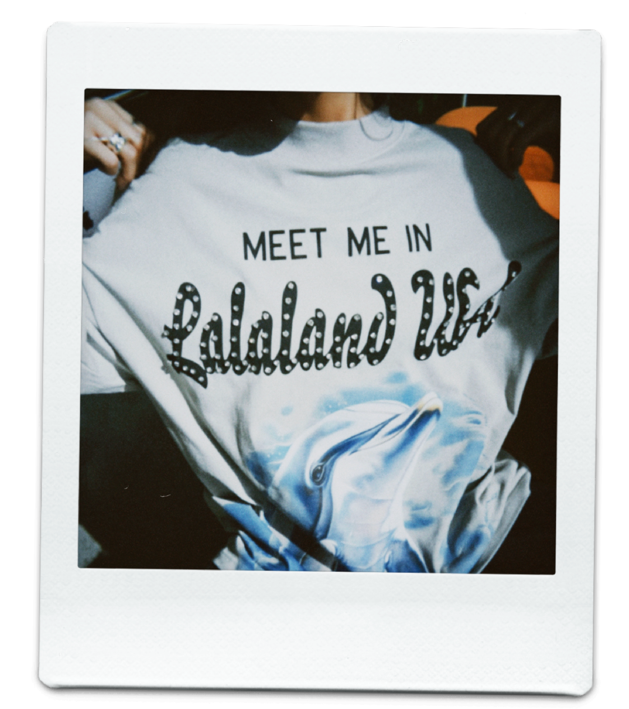 Close up polaroid photo of a girl wearing a "meet me in lalaland usa" t shirt with a dolphin on it