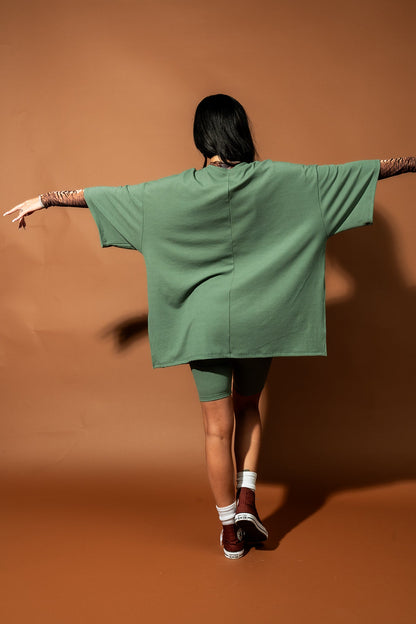 Girl/model standing against a brown backdrop wearing a sage green biker set with a tiger striped mesh top underneath