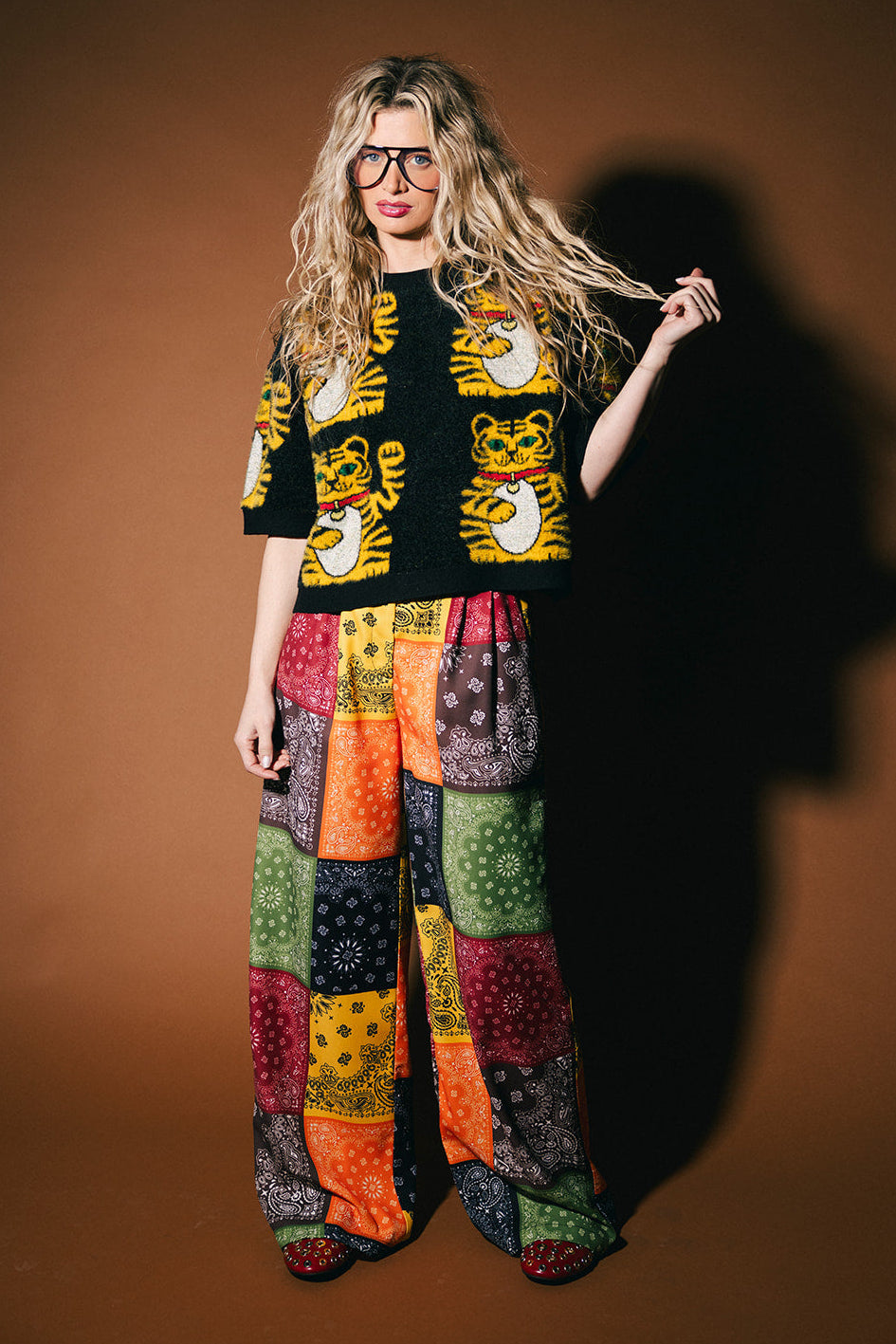 Person wearing a patterned sweater and colorful pants against a brown background