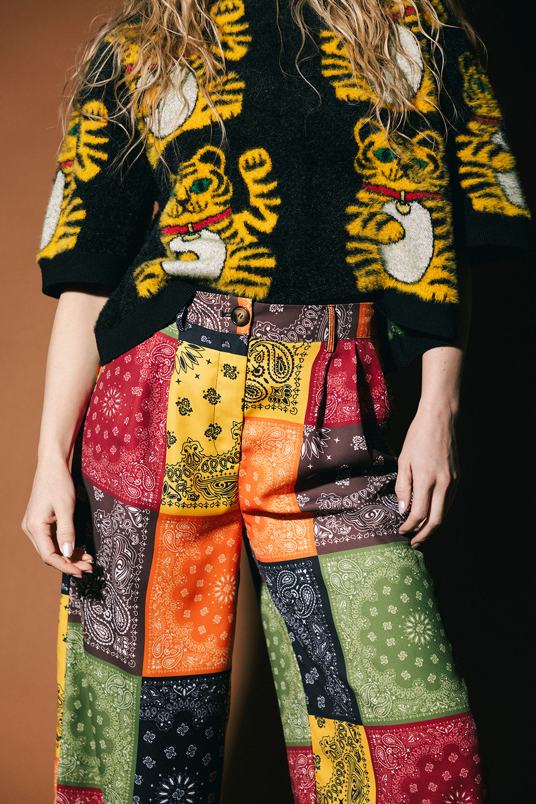 Person wearing a black sweater with tiger designs and colorful patchwork pants.