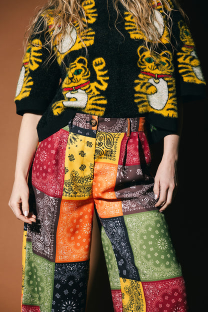 Person wearing a black sweater with tiger designs and colorful patchwork pants.
