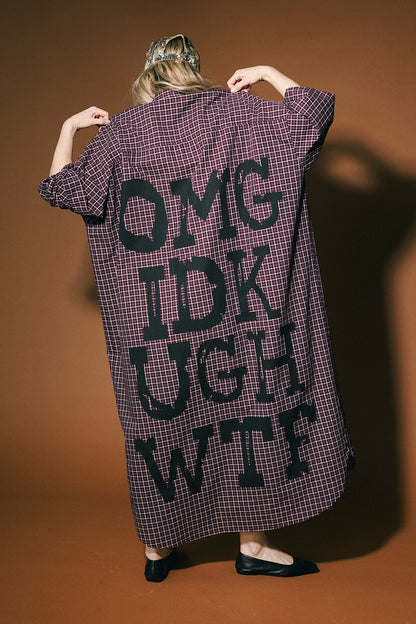 Person wearing a long, plaid duster with text on the back against a brown background