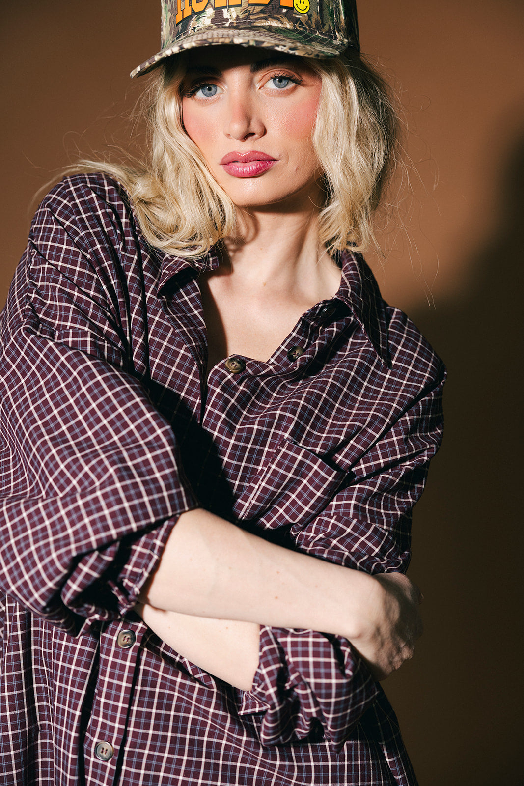 Woman wearing a plaid duster and cap against a brown background