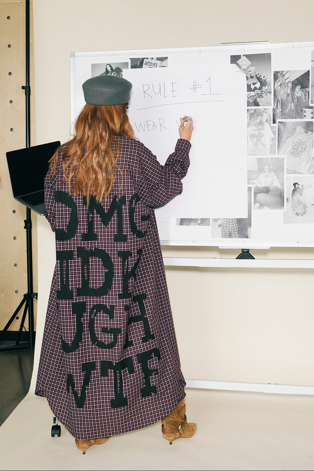 Person writing on a whiteboard with a long coat featuring text.