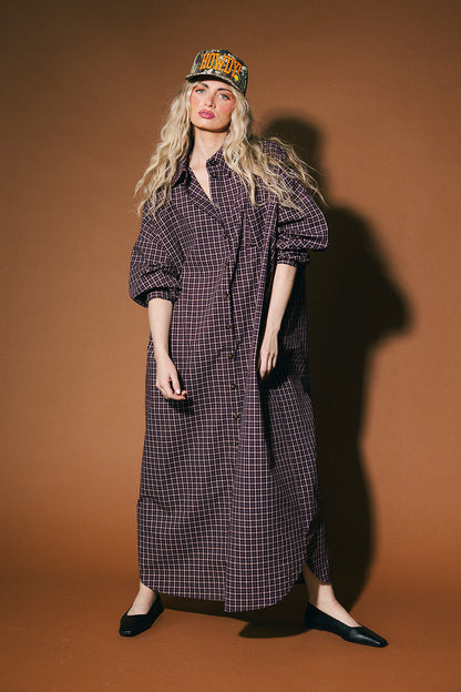 Woman wearing a long plaid duster and cap against a brown background