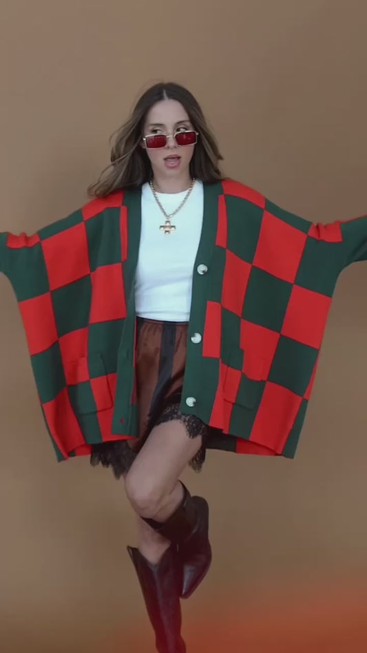 Video of a girl/model standing against a backdrop wearing a red and green checkered cardigan