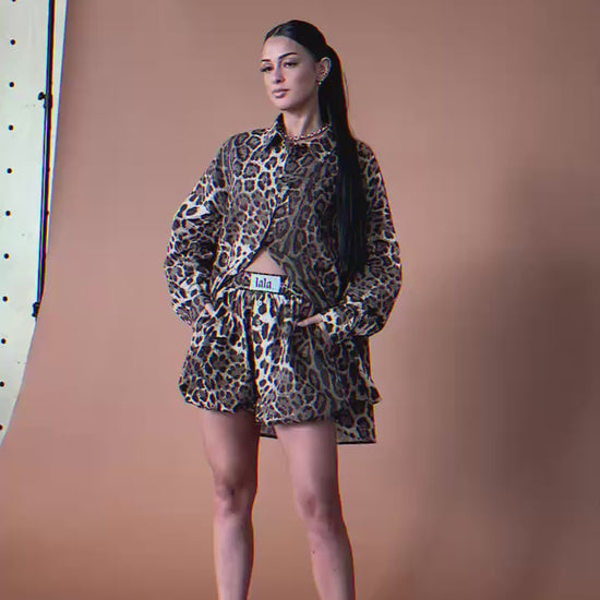 Video of woman wearing a leopard print button up and bloomer shorts against a brown backdrop.