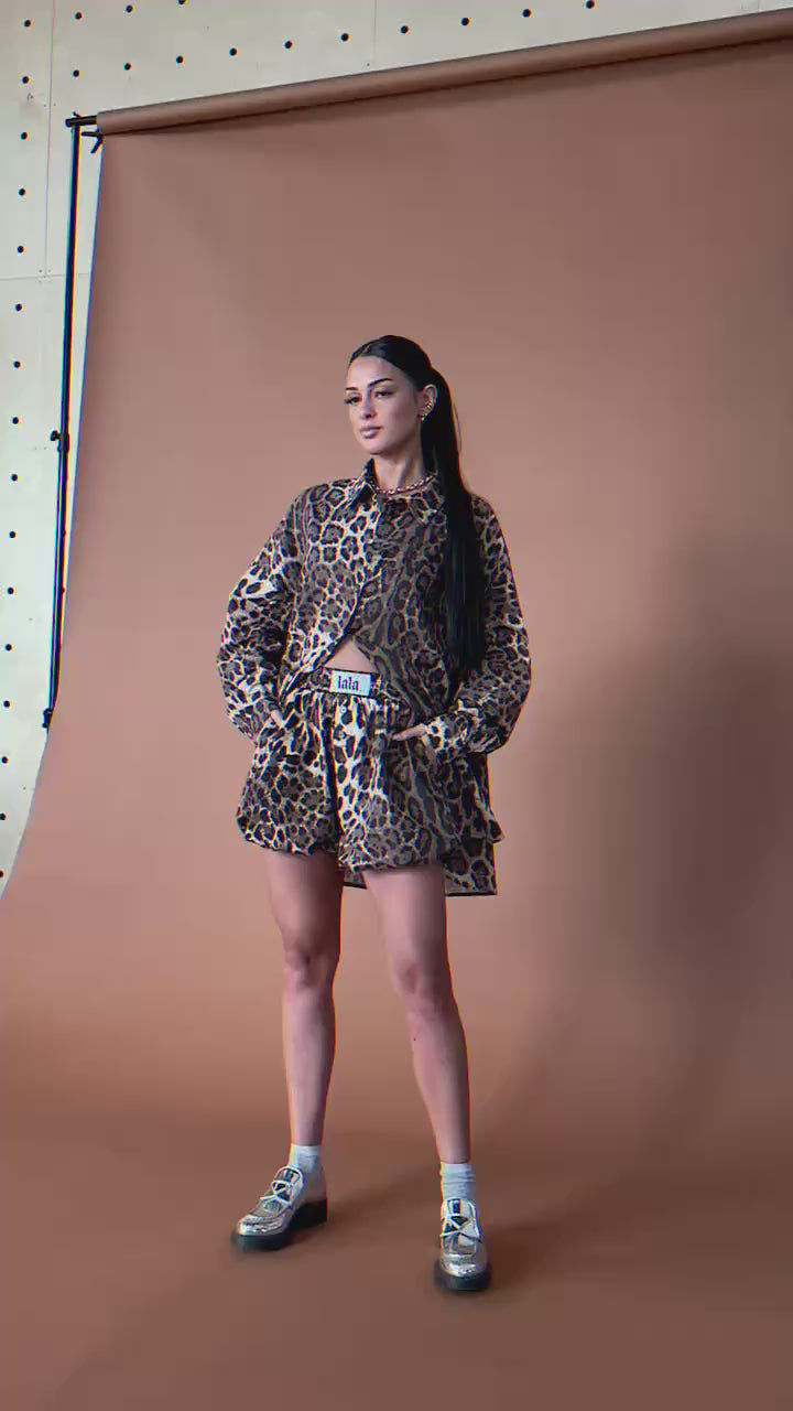 Video of woman wearing a leopard print button up and bloomer shorts against a brown backdrop.