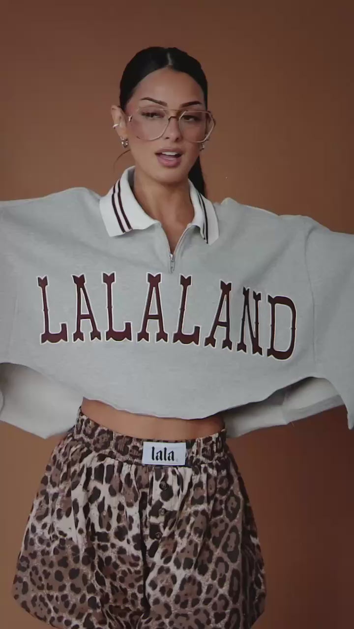 Video of woman wearing a grey cropped polo with "LALALAND" text against a brown backdrop.