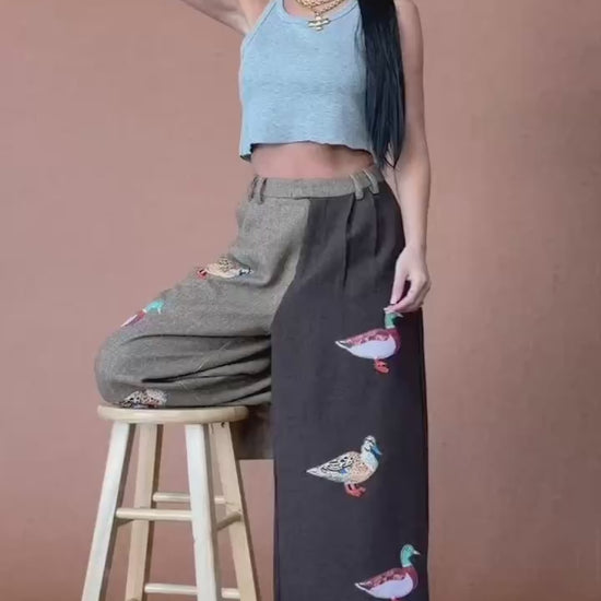 Video of woman wearing half and half trousers with duck patches against a brown backdrop.