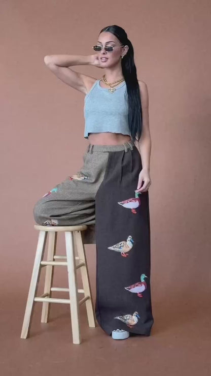 Video of woman wearing half and half trousers with duck patches against a brown backdrop.