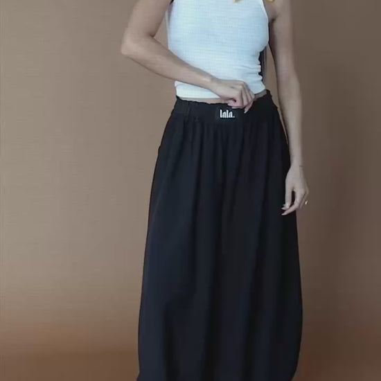 Video of woman wearing black bloomer pants against a brown backdrop.