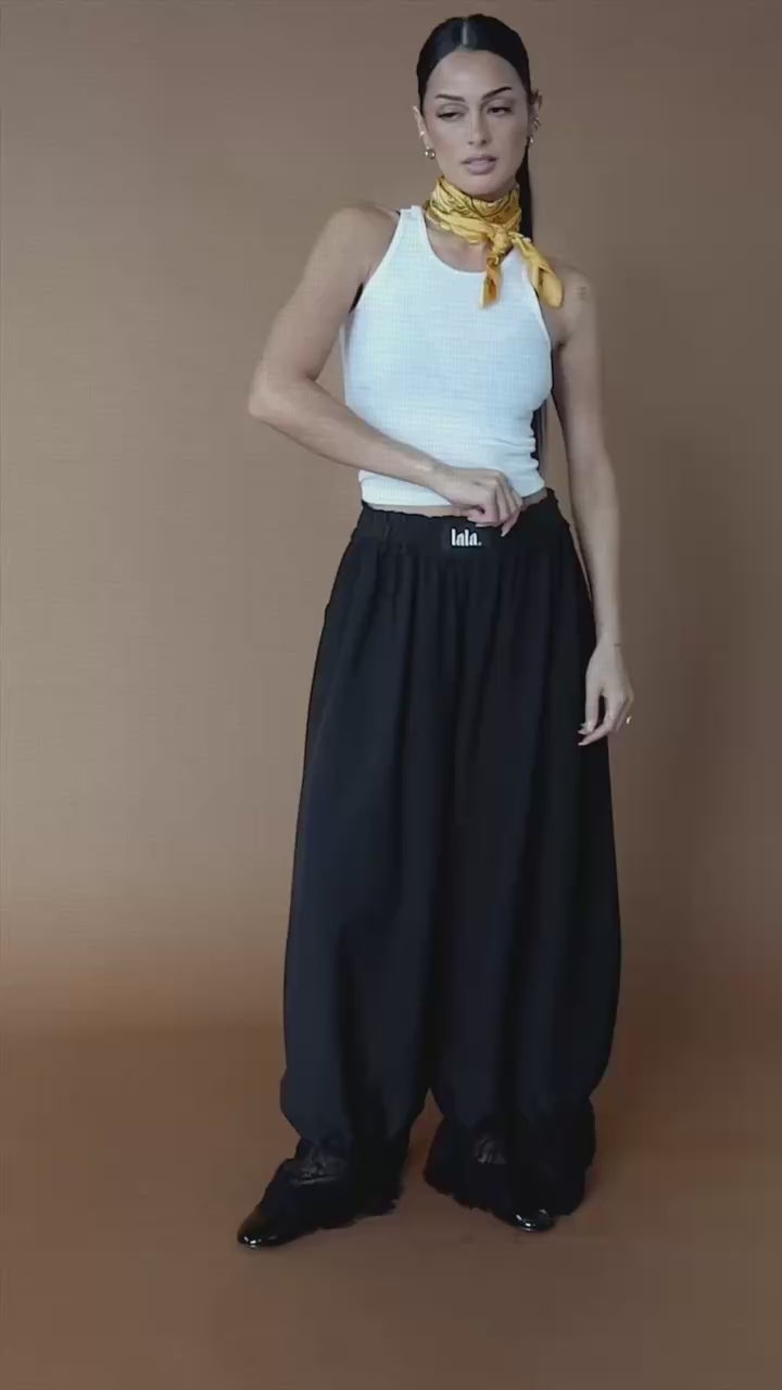 Video of woman wearing black bloomer pants against a brown backdrop.