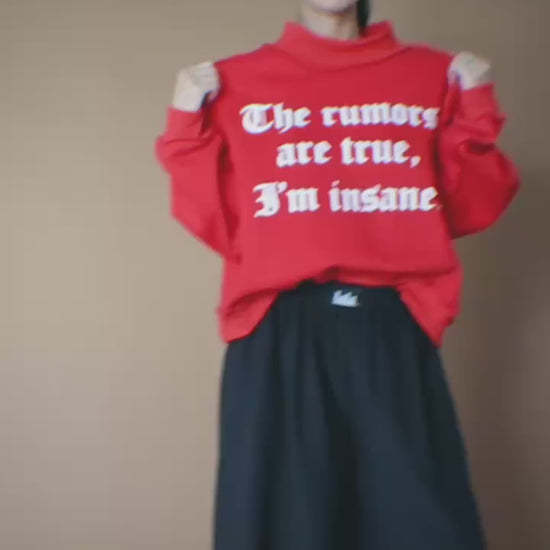 Video of woman wearing a red sweatshirt that says "The rumors are true, I'm insane." against a brown backdrop.