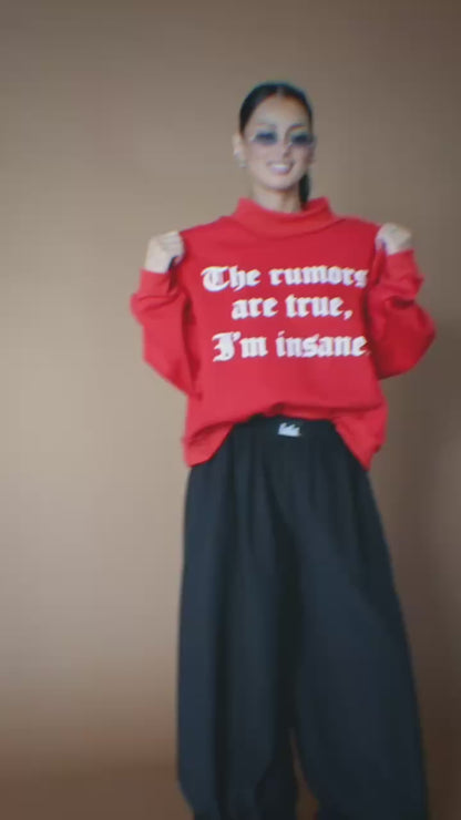 Video of woman wearing a red sweatshirt that says "The rumors are true, I'm insane." against a brown backdrop.