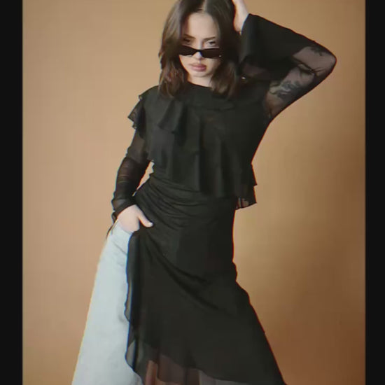 Video of a woman wearing a black asymmetrical ruffle tunic over blue jeans