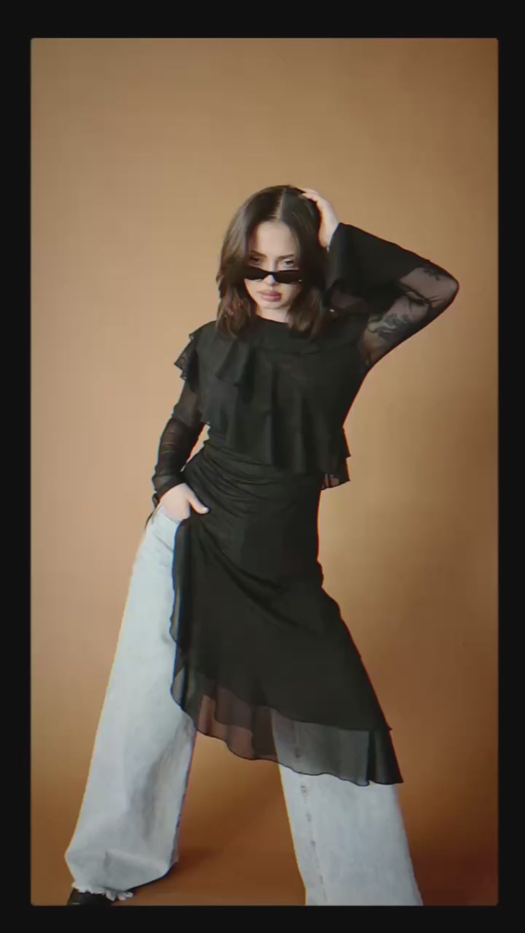 Video of a woman wearing a black asymmetrical ruffle tunic over blue jeans