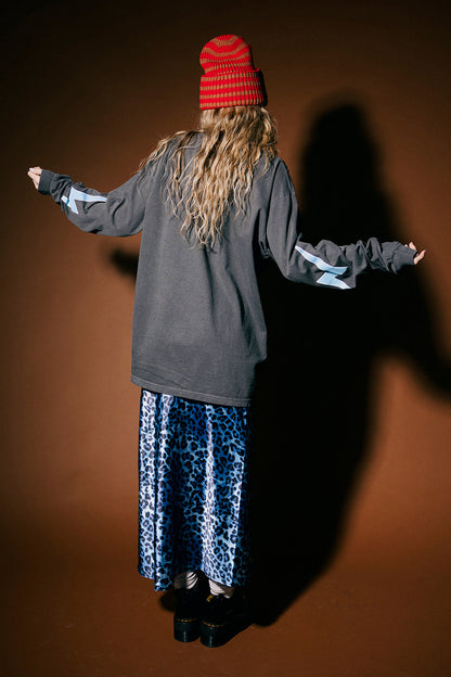 Person wearing a red beanie and gray hoodie with arms outstretched on a brown background